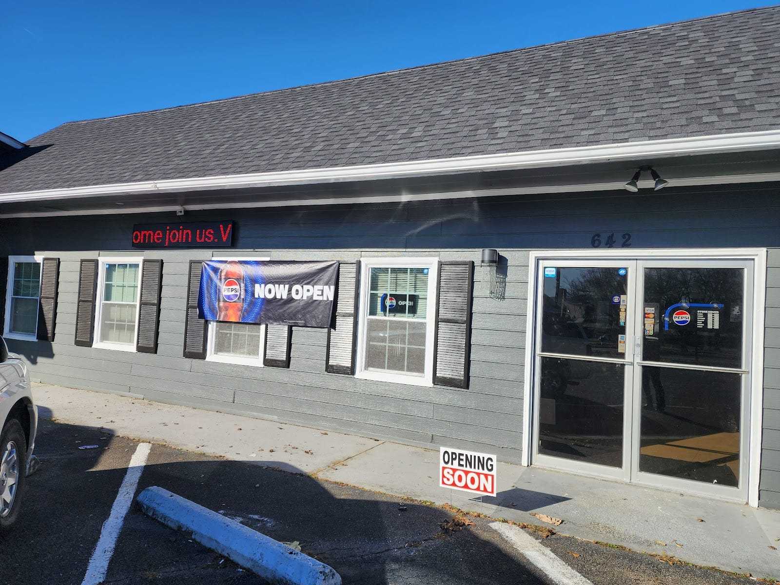 Storefront with "Now Open" and "Coming Soon" signs on a gray building.